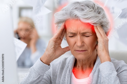 Elderly woman experiencing severe headache with red glowing pain zones on her temples and neck.