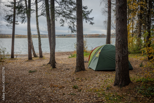 Bild auf Leinwand The tent stands alone in a forest clearing among the trees with a lake in the background