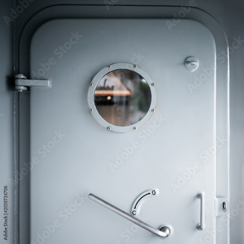 Heavy metal door with round porthole window and lever handle. Strong and secure void for naval ship design