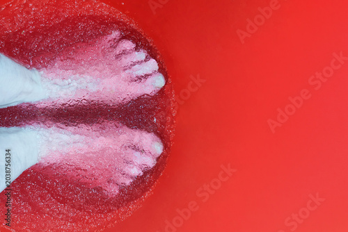 Feet in red basin with rose-scented gel and bubbles. Top view of foot spa treatment for relaxation and wellness at beauty salon or home self-care routine.