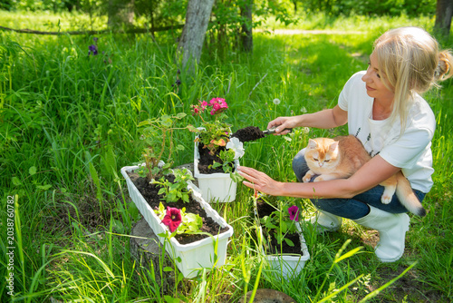 Woman planting flowers in garden with cat on lap enjoying sunny day