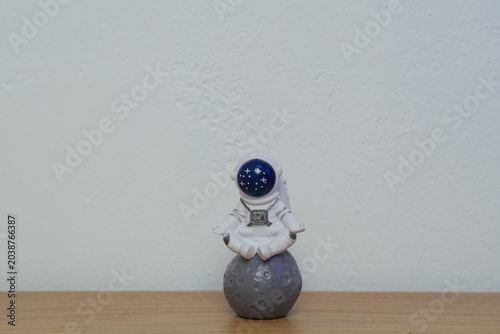 Cute miniature astronaut figurine meditating in lotus pose on top of a gray moon