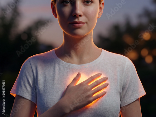 Woman placing hand over glowing chest with serene expression at sunset