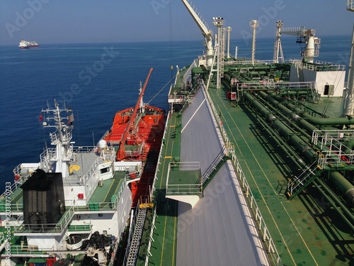 Schilderij op canvas A large liquefied gas carrier deck connects to a smaller red bunkering vessel on the open sea