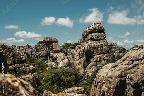 Eroded grey steep rock formations with some vegetation under a blue sky with some clouds. National Park of El Torcal de Antequera, Andalusia, Spain.