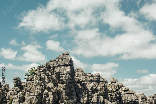 Eroded grey steep rock formations with some vegetation under a blue sky with some clouds. National Park of El Torcal de Antequera, Andalusia, Spain.