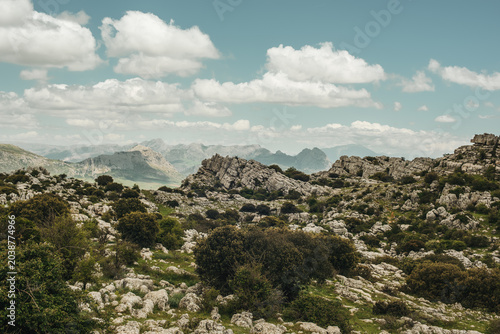 Eroded grey steep rock formations with some vegetation under a blue sky with some clouds. National Park of El Torcal de Antequera, Andalusia, Spain.