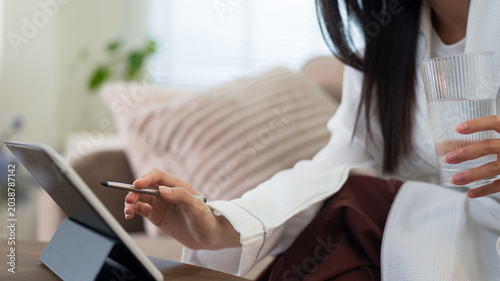 Foto Asian women drinking water holding glass using digital tablet stylus pen writing