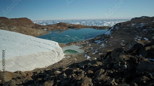 A rare Antarctic oasis with calm lakes and scattered stones set within a vast frozen landscape under a bright, clear sky.