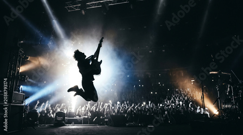 Musician silhouette jumping during guitar performance, high energy rock music moment, World Rock Day