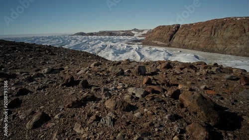 Antarctic scenery featuring an oasis with lakes and rocky terrain, with stones scattered across the landscape beneath a clear blue sky.