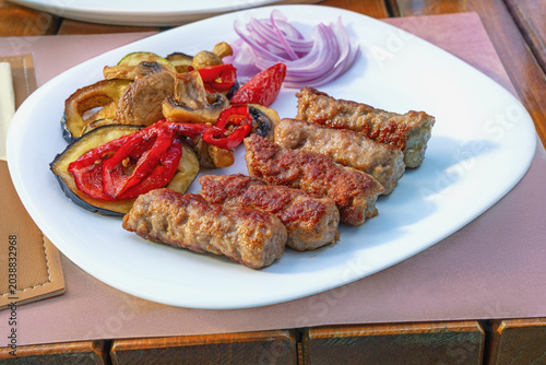 Balkan cuisine. Cevapi - grilled dish of minced meat - with vegetables. Selective focus