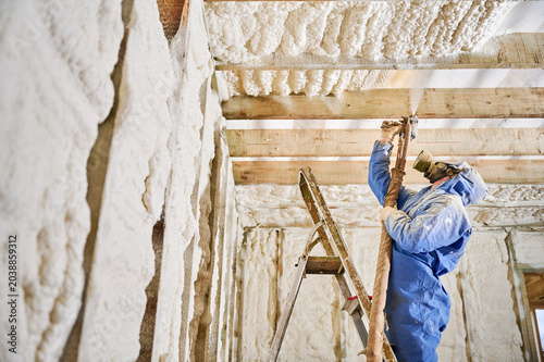 Contractor insulating ceiling beams and wall cavities with polyurethane foam spray. Residential building interior, airtight protection, renovation process and comfort concept.