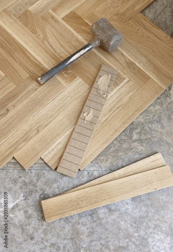 Beige parquet planks with adhesive and rubber mallet on floor during hardwood flooring installation