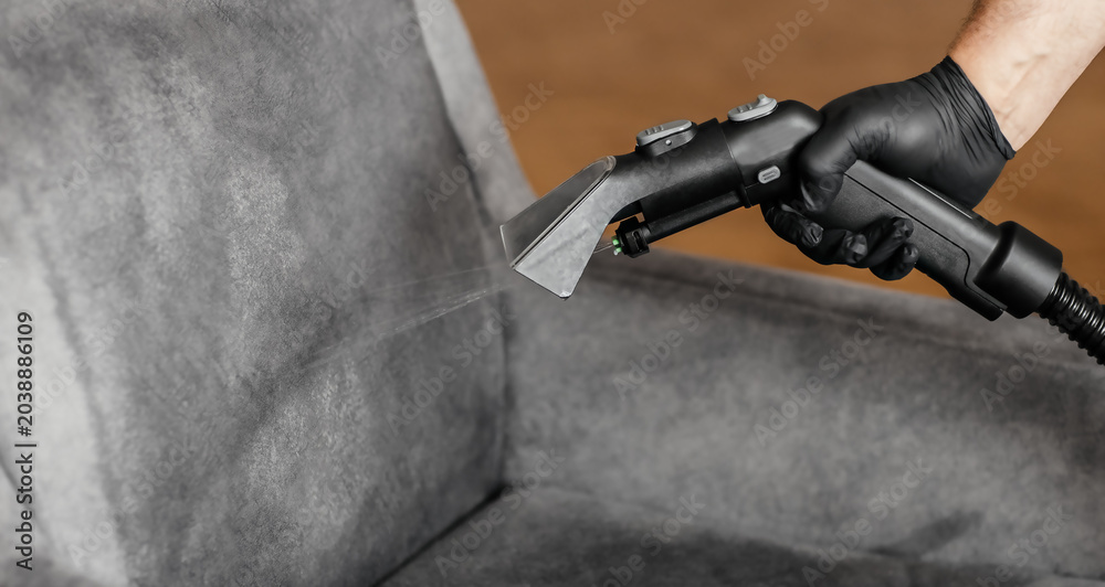 Fototapeta premium Professional upholstery cleaning with extraction vacuum cleaner spraying water on gray armchair