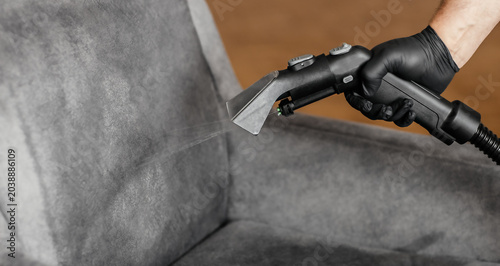 Professional upholstery cleaning with extraction vacuum cleaner spraying water on gray armchair