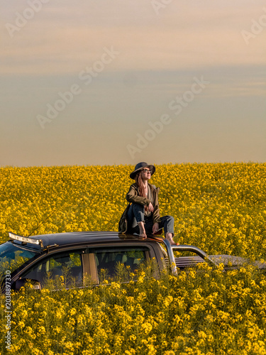 Woman Sitting on Pickup Truck Roof in Blooming Rapeseed Field at Sunset