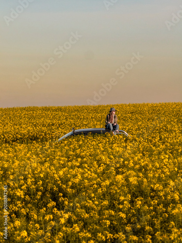Woman Sitting on Car Roof in Blooming Rapeseed Field at Sunset