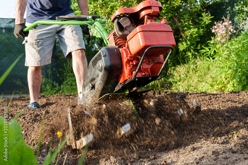 Quadro su tela Man using motor cultivator to loosen soil in garden close up