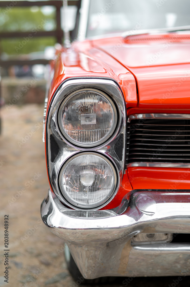 Fototapeta premium Close-up of the headlight of vintage car exhibition. Chrome trim and distinctive details of American automotive design.