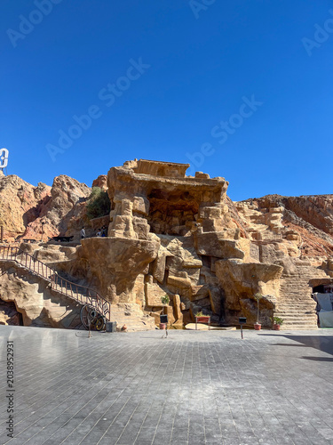 Obraz na plátně Large artificial rock formation featuring carved stone architecture and stairways beneath a clear blue sky