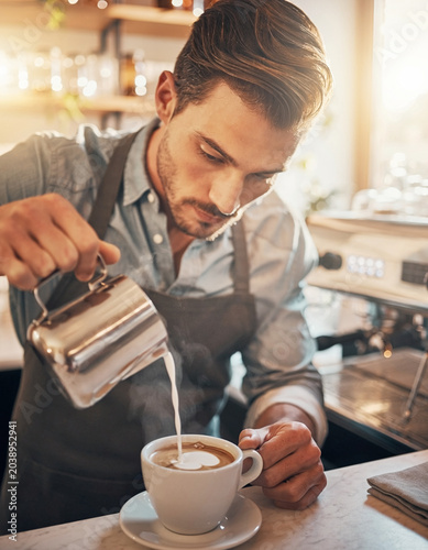Professional barista pouring milk into coffee cup creating latte art, handsome male worker preparing hot beverage in cafe counter