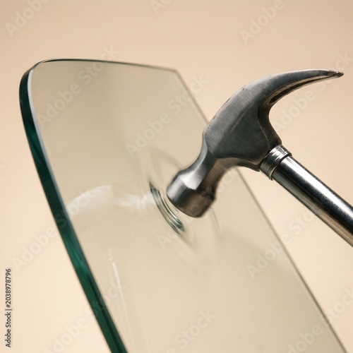 Metal hammer striking tempered safety glass sheet demonstrating impact resistance