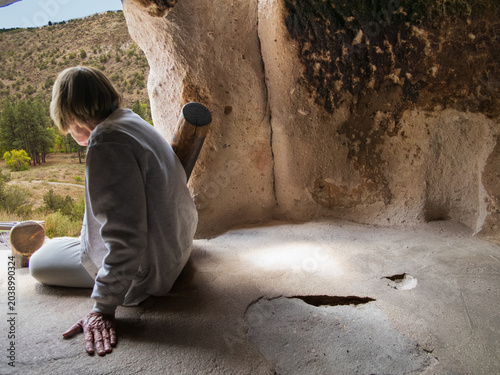 Fényképezés Bandelier National Monument, May 6, 2026 - A woman looks out from a prehistoric Puebloan cave dwelling looking out as an ancient Puebloan may have done
