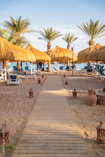 Foto Wooden pathway leads through a beach resort in Sharm El Sheikh Egypt with palm trees straw umbrellas and sandy coastline