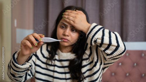 Indian Woman Checking Fever with Thermometer While Sick in Bed at Home