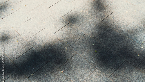 High angle texture view of granite paving tiles on a city sidewalk with dark soft shadows from trees on a sunny day.