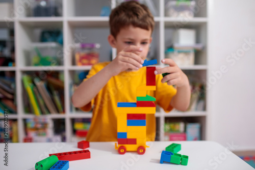 Concentrated boy carefully placing blocks on tower, deeply concentrated on construction process, concentrated preschooler building colorful structure in kindergarten playroom