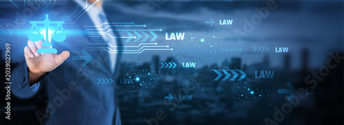 Legal technology concept. Businessman touching a digital justice scale icon on a futuristic blue tech background with 