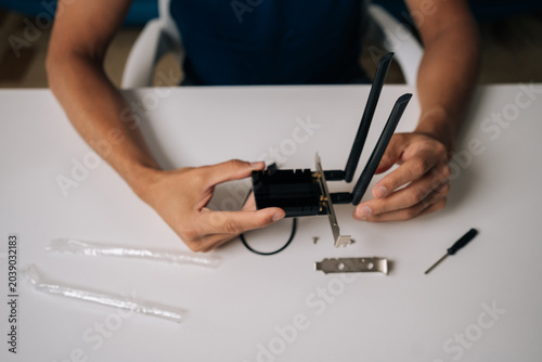 Close-up top view of technician hands assembling wi-fi module on white table, using small screwdriver and other components for computer upgrade or repair. Concept of desktop PC maintenance and service
