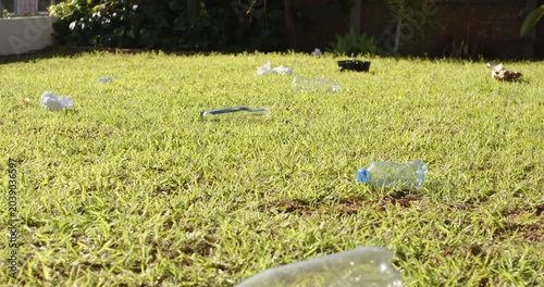 Camera pulling back is revealing crushed bottle and litter across sunny yard, showing extent