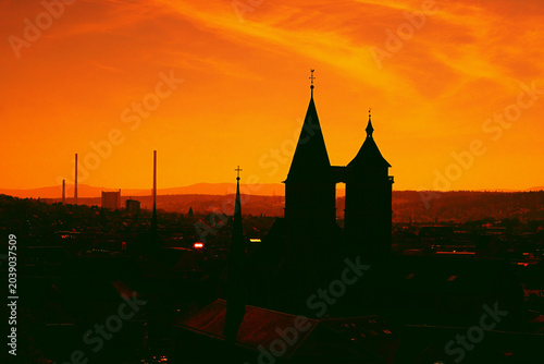The dark shilouettes of a big, old church and a big town below a colourful sundown