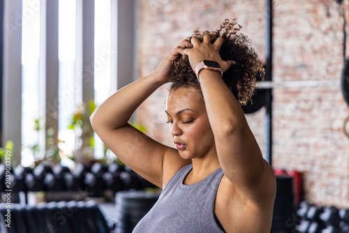 Foto African American woman pulling curly hair into ponytail in gym by dumbbell rack,