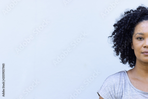 African American woman posing against pale blue-gray wall in studio, wearing gray top, copy space