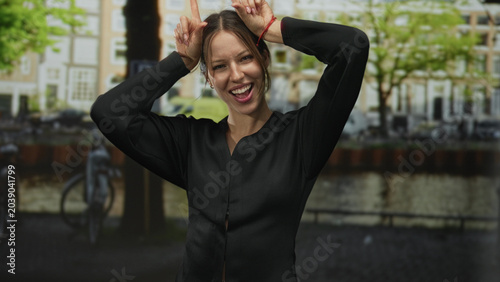 Photography Woman showing horns gesture with hands and smiling face on a street in amsterdam; playful mischief moment
