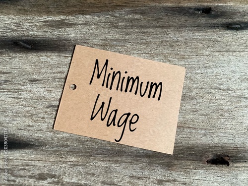 Obraz na plátně The phrase Minimum Wage written on a plain cardboard label against a rustic wood background, symbolising labor economics and base salary issues