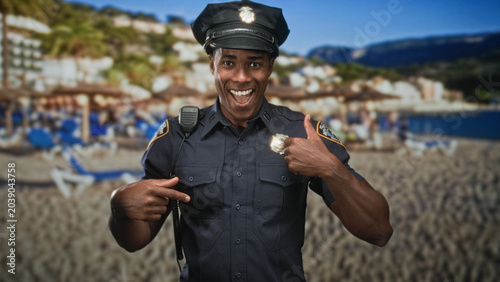 Obraz na płótnie Man police officer smiling and pointing finger to chest while pointing to shiny badge, wearing radio mic and cap with blurred beach backdrop in studio; pride service