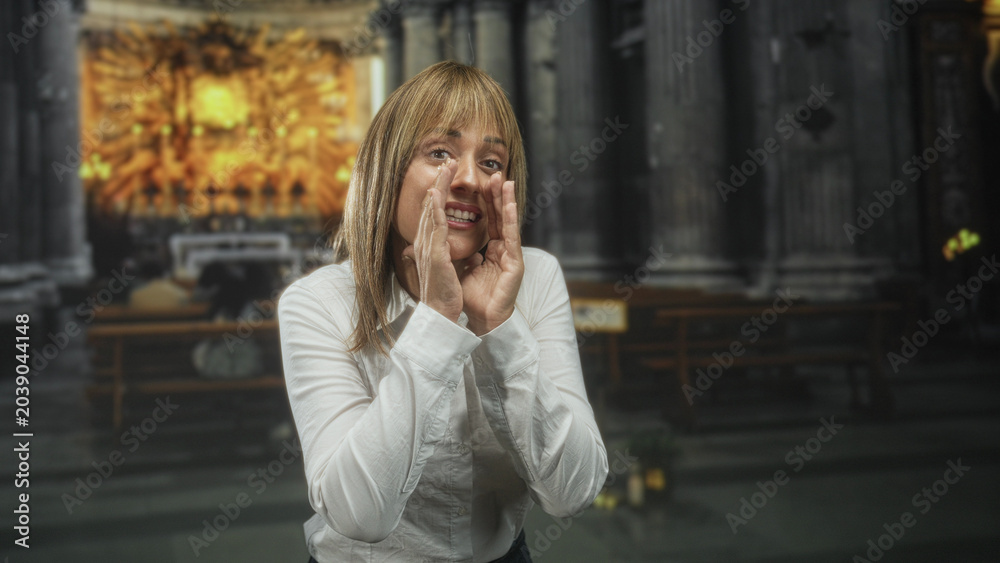 Fototapeta premium Woman cups hands and shouts while smiling, white shirt, standing before an ornate altar inside a church building; joyful devotion.