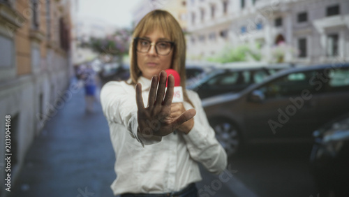 Bild auf Leinwand Woman holding a microphone with palm extended to camera during a street interview; assertive reporting