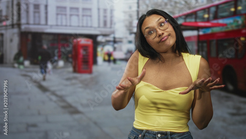Foto Woman shrugging with palms up and slight smirk on a london street beside red doubledecker bus and phone booth; nonchalant