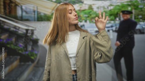Fotografija Woman redhead showing ok hand gesture with visible hand at building entrance on street near steps and parked cars; casual confidence