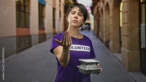 Foto Woman volunteer holding stacked foil food containers, beckoning with an outstretched hand in a narrow street lined with arches and buildings; pleading help request