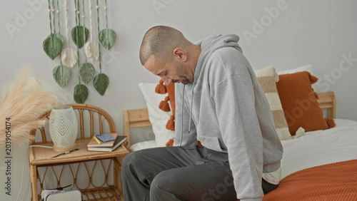 Bild auf Leinwand Man sitting on bed in studio with hand on head gripping temple after waking, showing pained expression and restless posture; pain