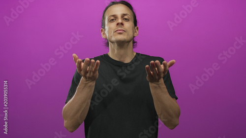 Fotografía Man with long hair and open palms showing hands in a purple studio wearing black t shirt, facing camera and gesturing with both hands; pleading for help