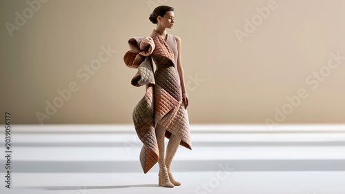 Ein Model trägt ein asymmetrisches Kleid aus mehrschichtigen, gestreiften Stoffelementen in Erdtönen.
