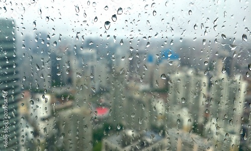 Tableau sur toile Raindrops on glass windowpane with blurry cityscape view in a rainy day